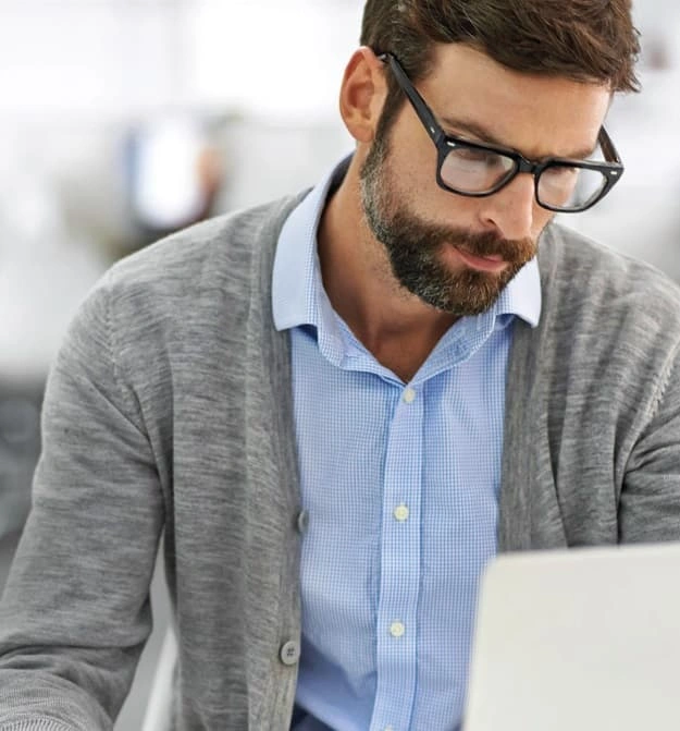 Male With Glasses Looking Down At His Computer, In The Office Exporting Expenses To Business Central In The Cloud